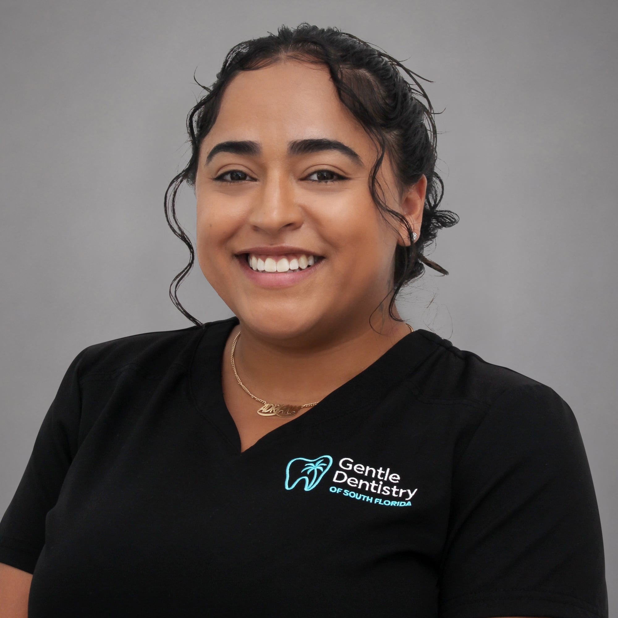 Headshot of a smiling female healthcare professional with dark pulled-back hair wearing a black Gentle Dentistry logo scrub top