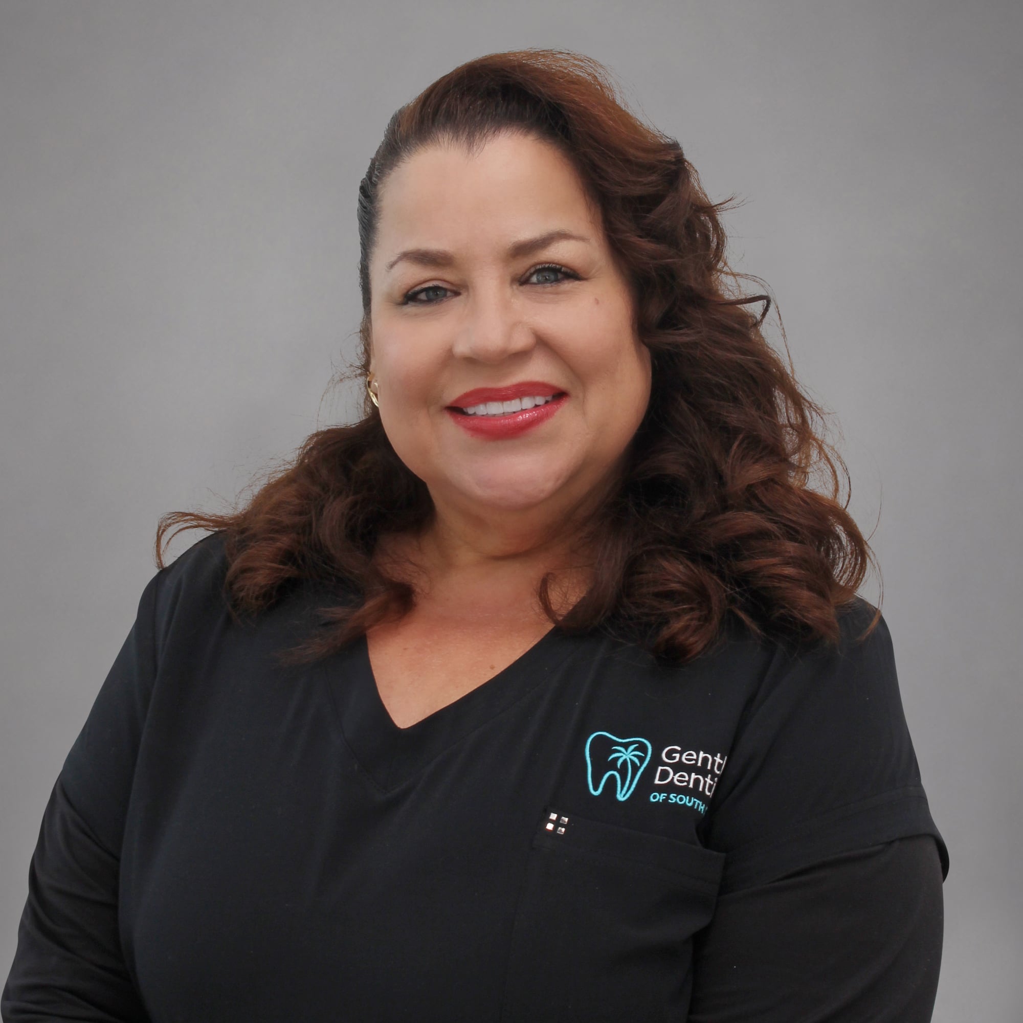 Portrait of a smiling woman with wavy reddish-brown hair wearing a black Gentle Dentistry V-neck scrub top