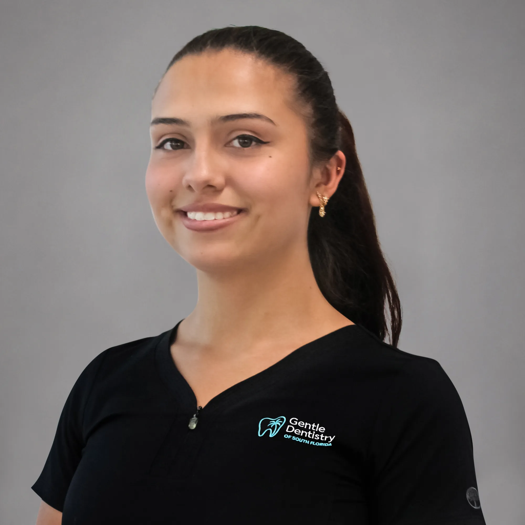 Headshot of a smiling young woman with dark hair tied back in a ponytail wearing a black Gentle Dentistry scrub top