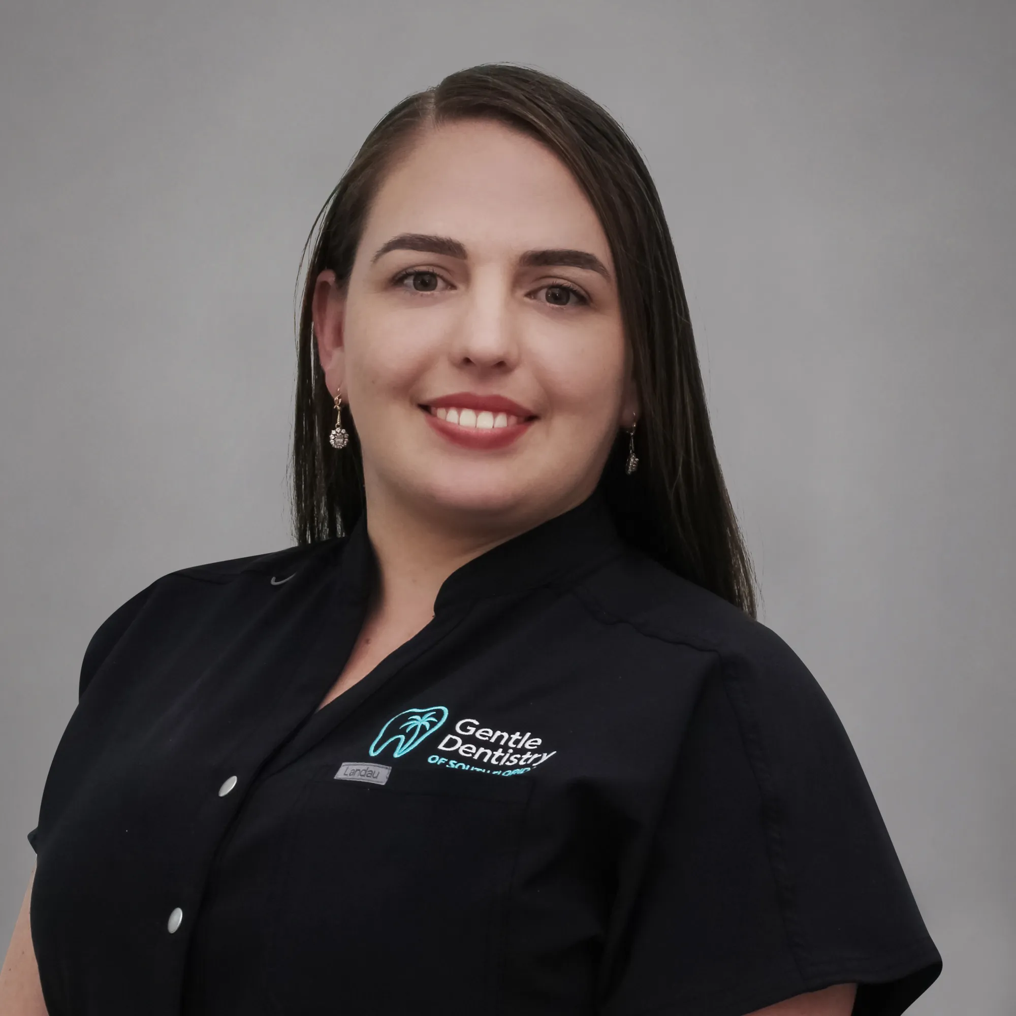 Studio headshot of a smiling female staff member with long dark hair wearing a black branded uniform top